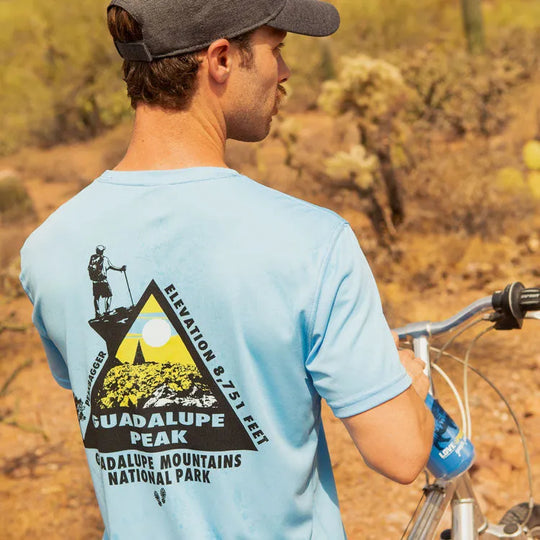 Front view of nan in performance T-shirt standing with his bike on a desert trail