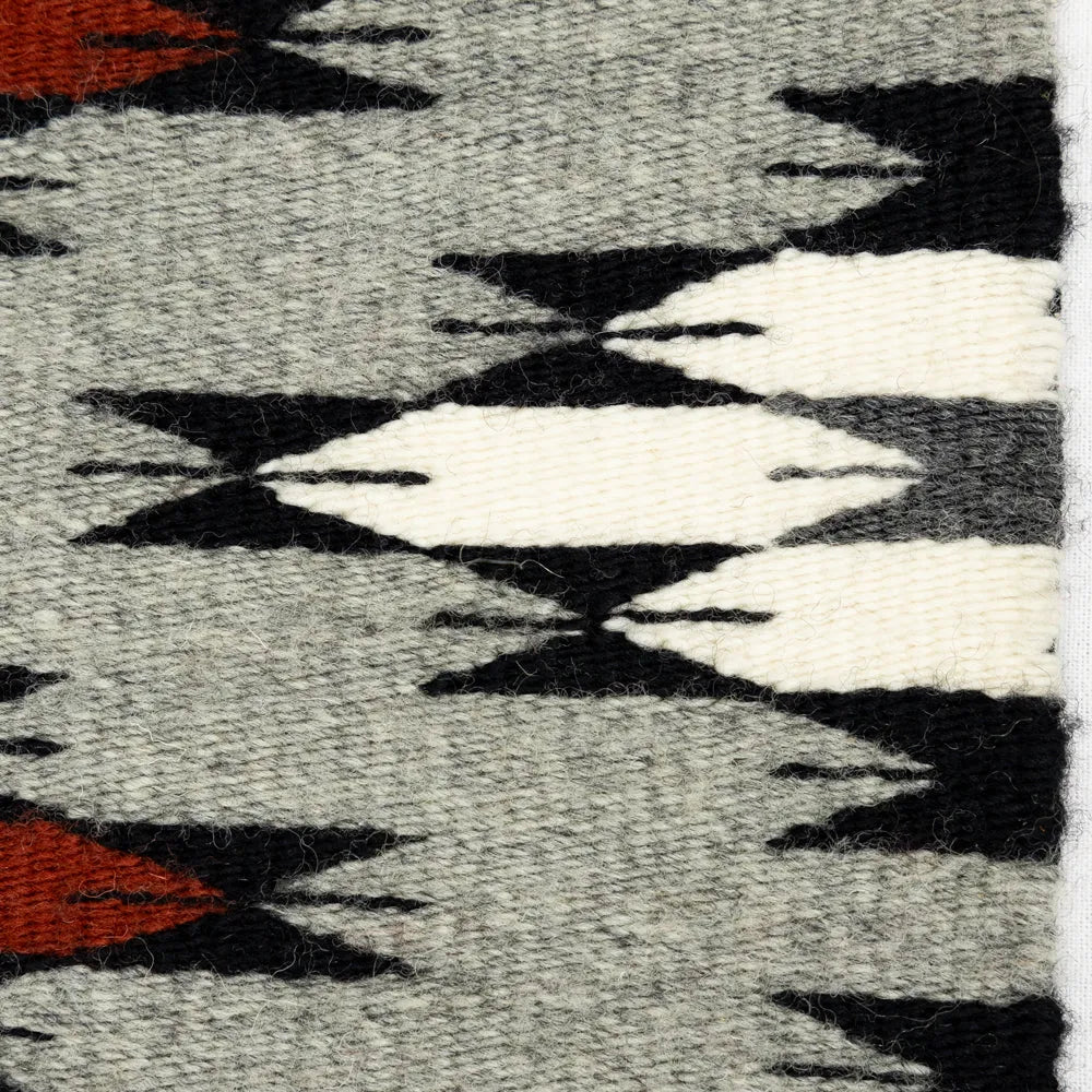 Close-up of a patterned Navajo textile with black, white, and red shapes on a gray background