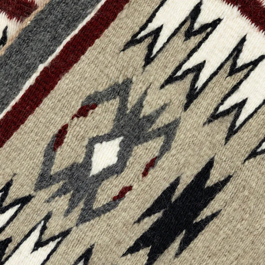 Close-up of a patterned fabric with geometric designs in black, white, and red on a beige background.
