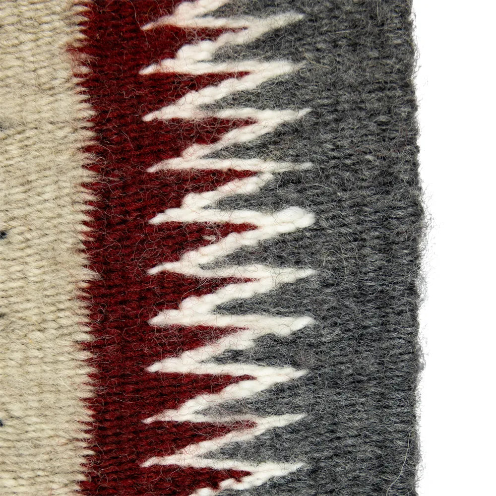 Close-up of a the edge of Navajo weaving with red, gray, and white patterns.