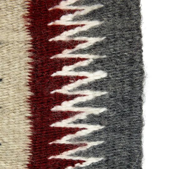 Close-up of a the edge of Navajo weaving with red, gray, and white patterns.