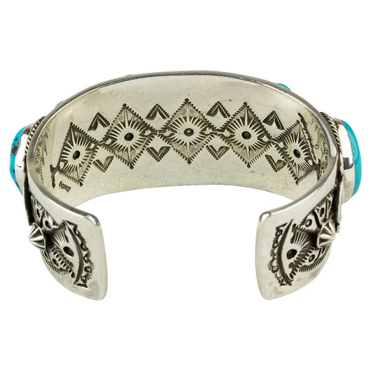 Silver bracelet with geometric patterns on inside of cuff placed on a white background
