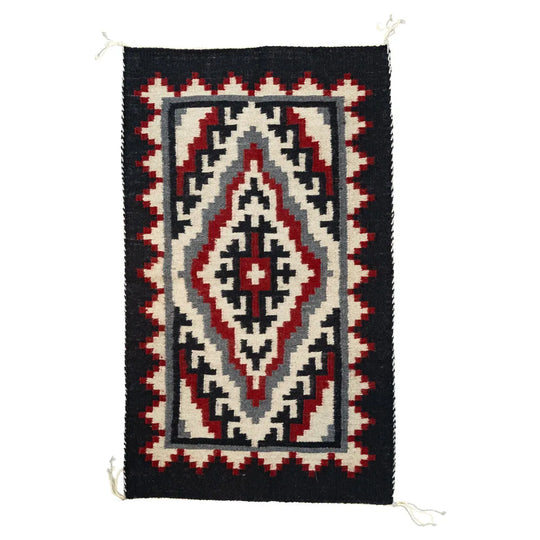 Woven Navajo rug with geometric pattern on a white background