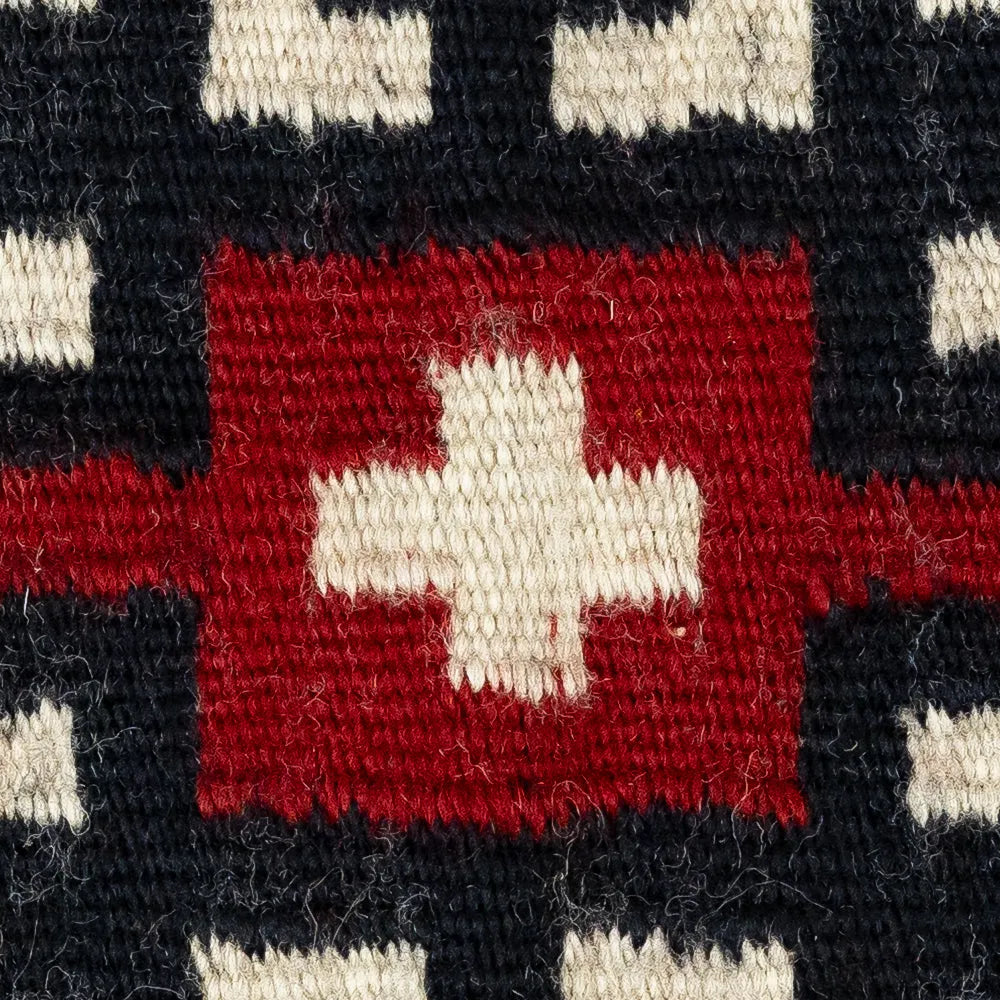 Close-up of a woven fabric with a red square and white cross pattern on a black background.