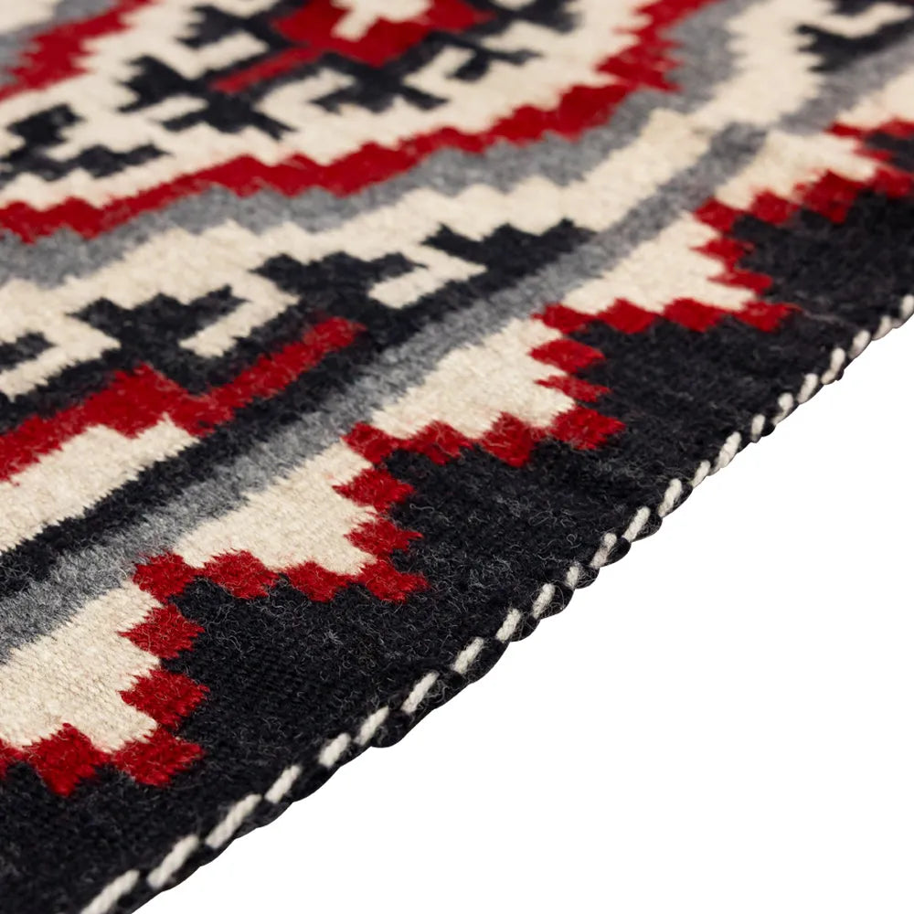 Close-up of a patterned rug with red, black, and white colors on a white background.