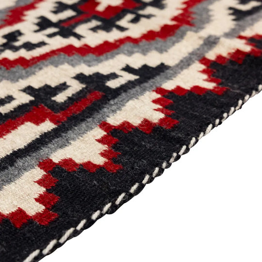 Close-up of a patterned rug with red, black, and white colors on a white background.
