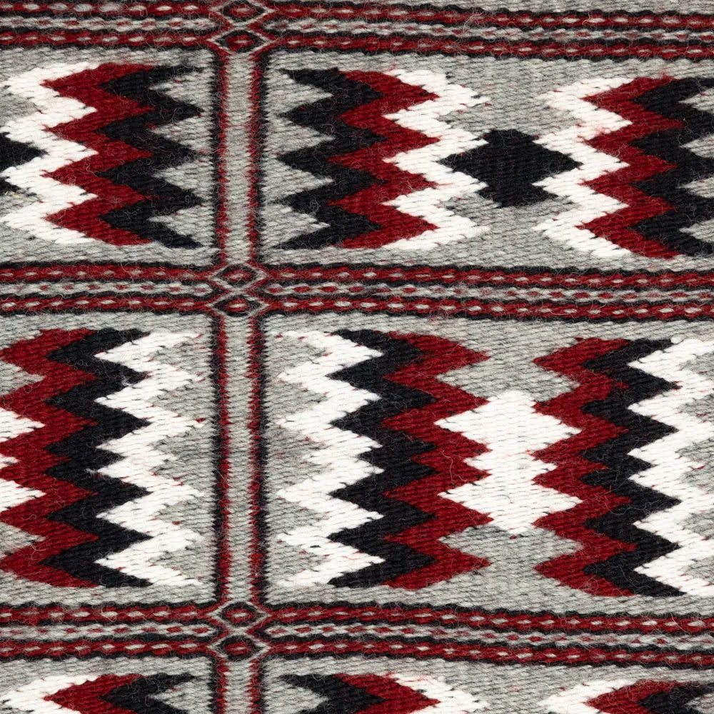 Close-up of a patterned fabric with red, black, and white colors on a gray background.