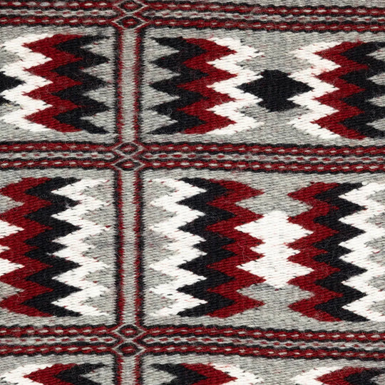 Close-up of a patterned fabric with red, black, and white colors on a gray background.