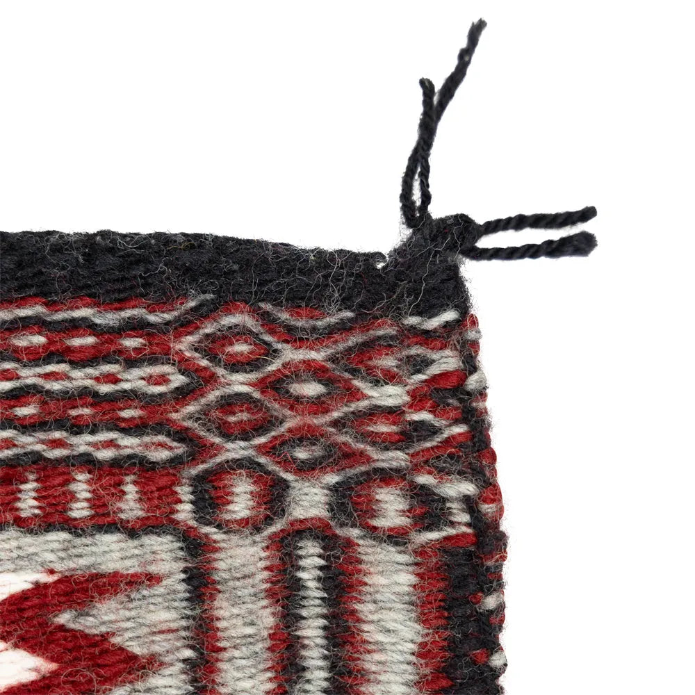 Corner detail of Navajo rug with red, white, and black patterns.