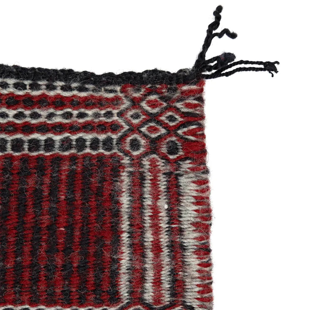 Close-up of a woven textile with red, black, and white patterns on a white background