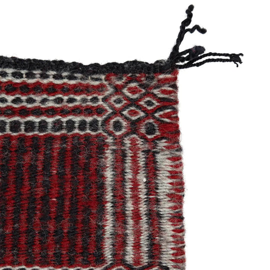 Close-up of a woven textile with red, black, and white patterns on a white background