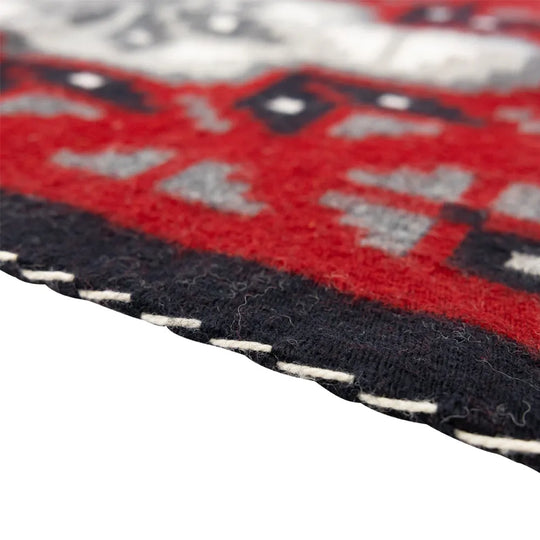 Close-up of a red, black, and gray patterned fabric with white stitching on a white background.