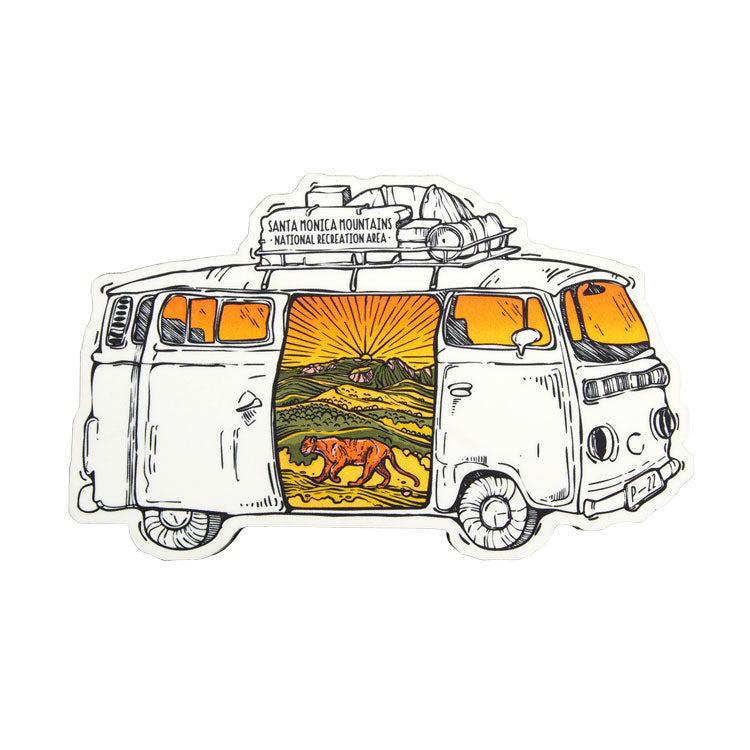 A magnet featuring an illustration of a vintage RV with a mountain lion and a sunset depicted through the open door.