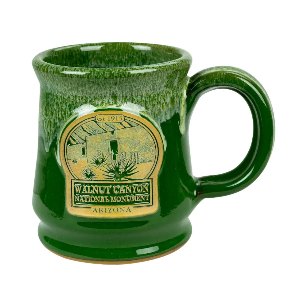 A green glazed ceramic mug featuring a gold-colored oval emblem for Walnut Canyon National Monument, Arizona, shown on a plain white background.