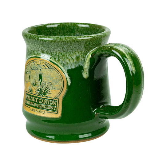 A green glazed ceramic mug with a handle, featuring a gold-colored &