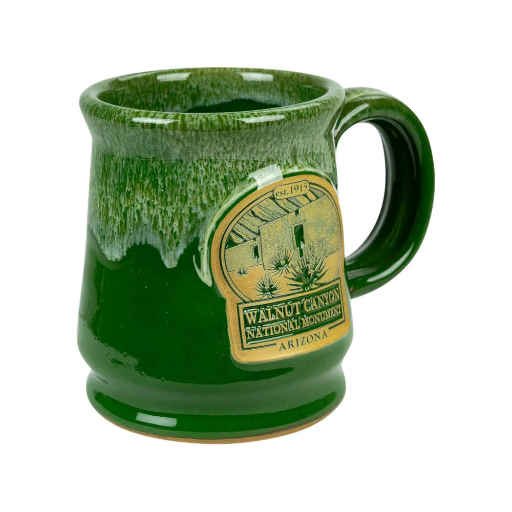 A green glazed ceramic mug featuring a gold-colored oval emblem for Walnut Canyon National Monument, Arizona, shown on a plain white background.