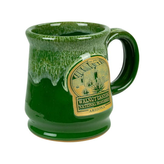 A green glazed ceramic mug featuring a gold-colored oval emblem for Walnut Canyon National Monument, Arizona, shown on a plain white background.