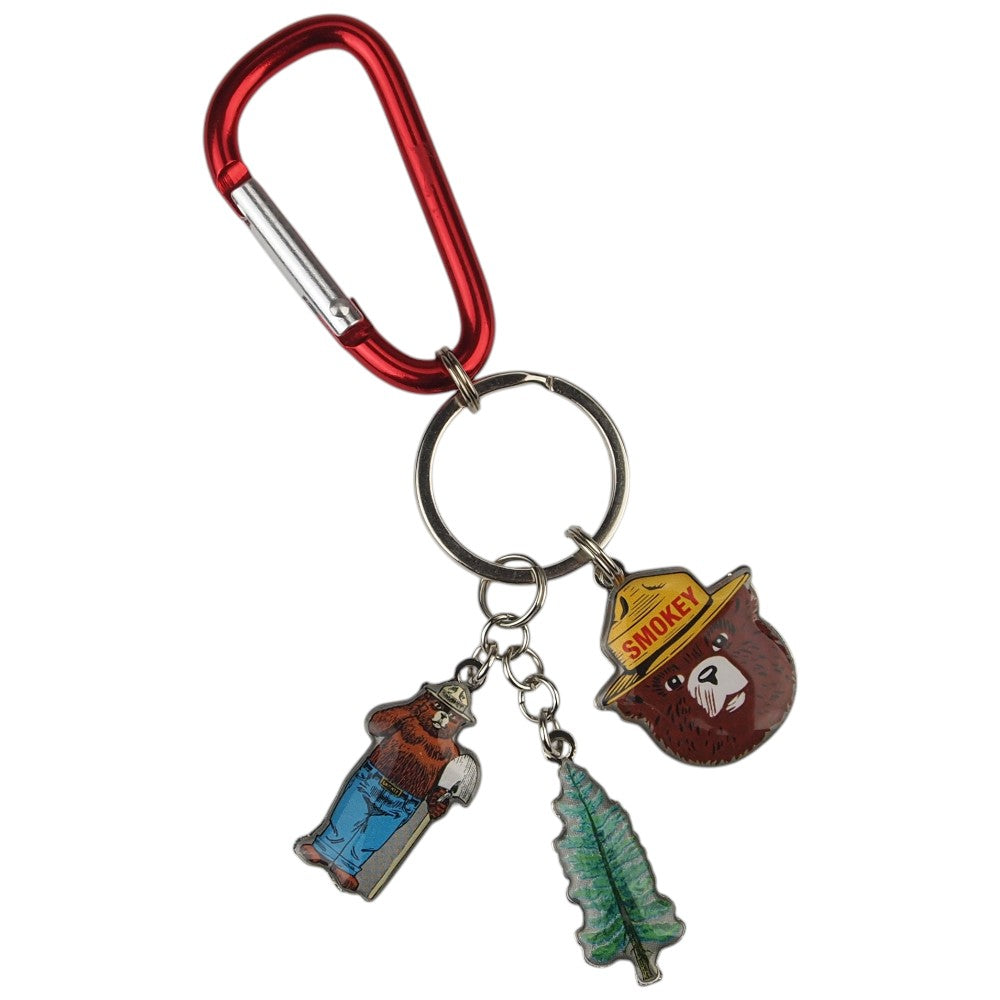 A red carabiner keychain with three dangling charms: a Smokey the Bear head charm, a Smokey with shovel charm, and a pine tree charm, shown on a plain white background.