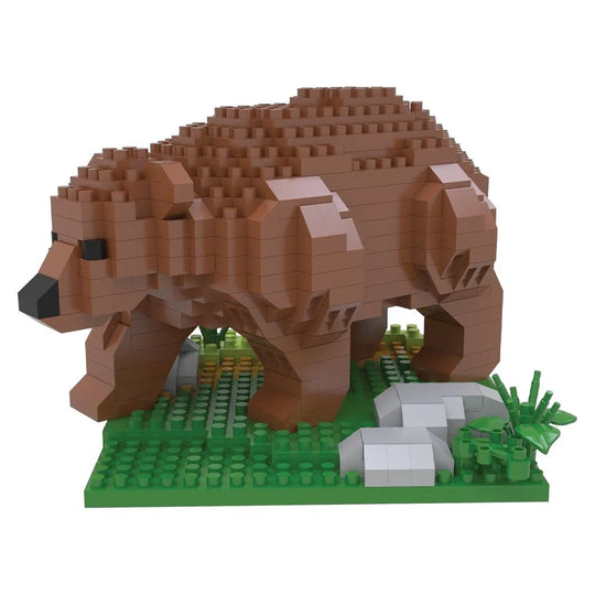 A grizzly bear building block model constructed from small interlocking bricks, standing on a green base with small gray rocks and green foliage details, isolated on a white background.
