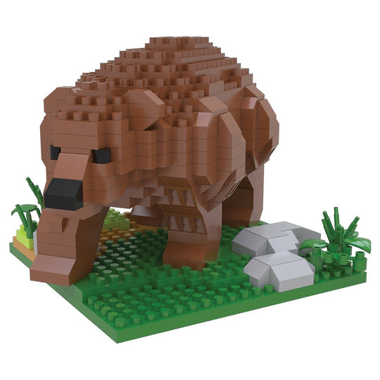 A block-style toy animal figure resembling a brown grizzly bear built from interlocking bricks, standing on a green base with grass and gray rocks, photographed on a plain white background.