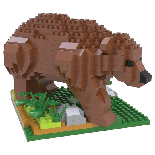 A block-built toy bear model made of brown bricks, standing on a green base with small plant and rock details, photographed on a plain white background.