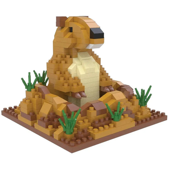 A toy building-block model of a prairie dog sitting on a rocky base with small green grass pieces, photographed on a plain white background.