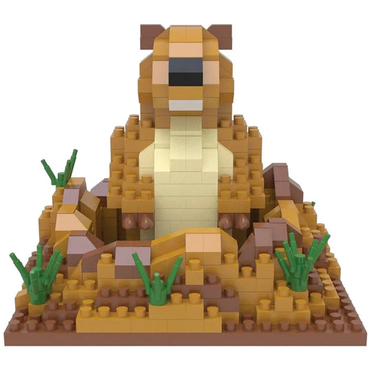 A block-built toy model of a prairie dog constructed from interlocking bricks, featuring a light tan body, darker brown ears and legs, green grass accents, and a brown base, shown against a plain white background.