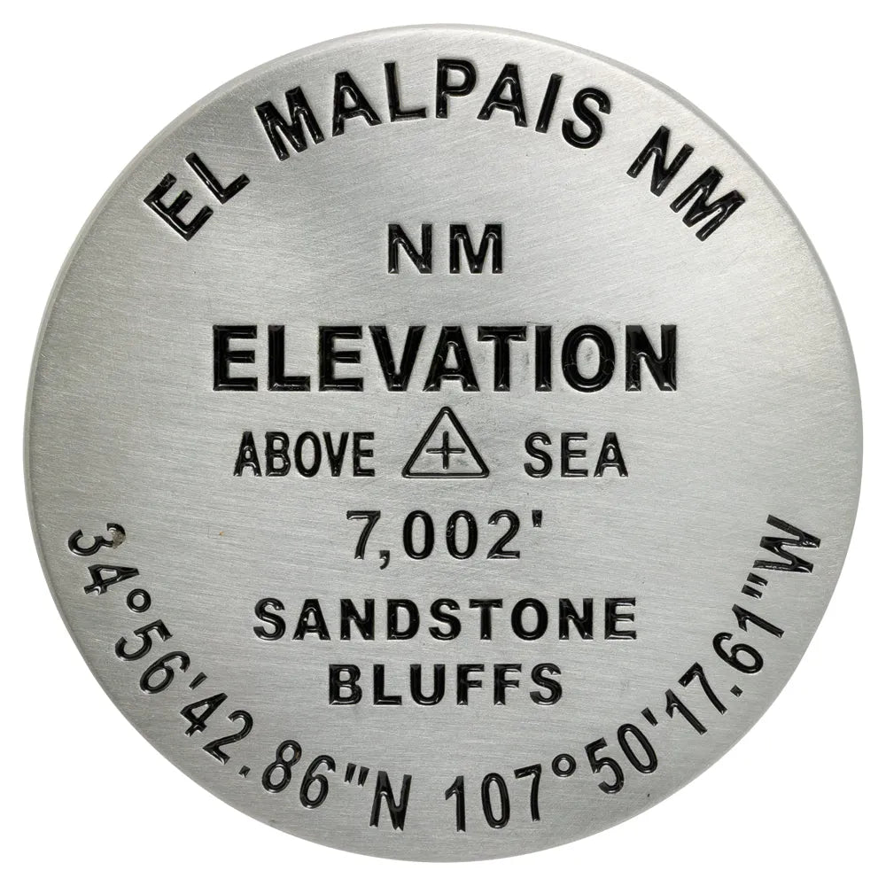 A round metallic elevation marker plaque for El Malpais NM, showing engraved text including &