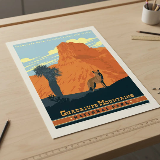 A vintage-style travel poster for Guadalupe Mountains National Park, featuring an orange rock formation, a blue sky, a palm tree, and a coyote, lying flat on a drafting table.