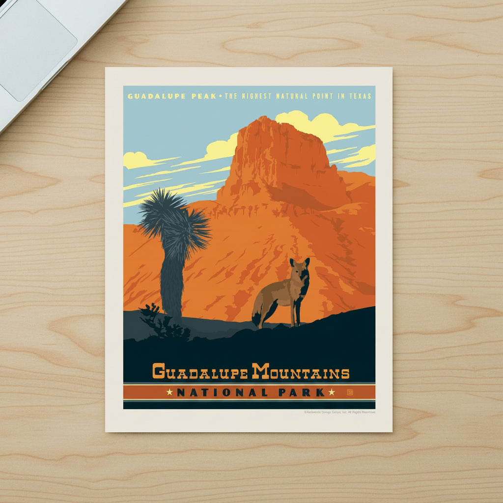 A vintage-style travel poster for Guadalupe Mountains National Park, featuring an orange rock formation, a blue sky, a palm tree, and a coyote, lying flat on a desk.