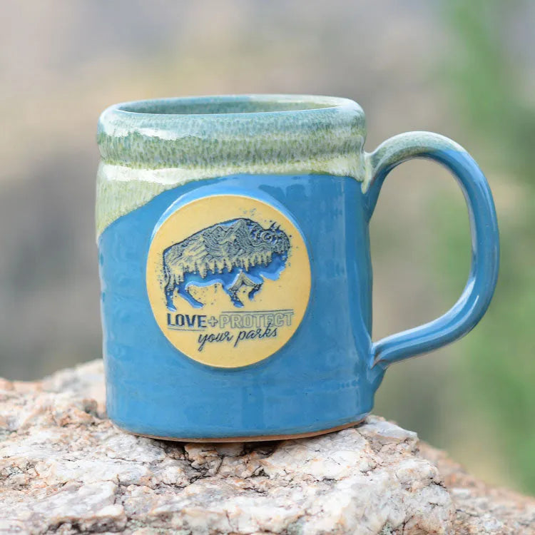Love + Protect Your Parks® Camper Mug on a rock out in nature