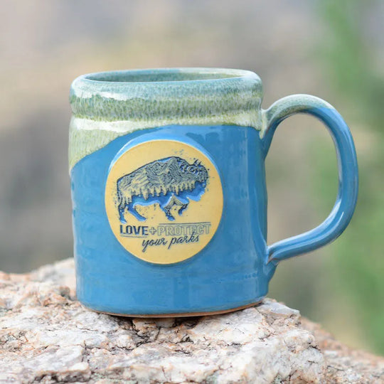Love + Protect Your Parks® Camper Mug on a rock out in nature