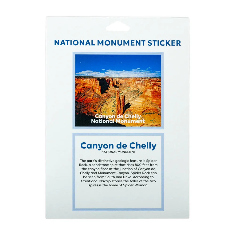 A National Monument Sticker for Canyon de Chelly National Monument, presented on its white backing card. The card features a colorful landscape photo of the canyon and a text box with historical details about Spider Rock.