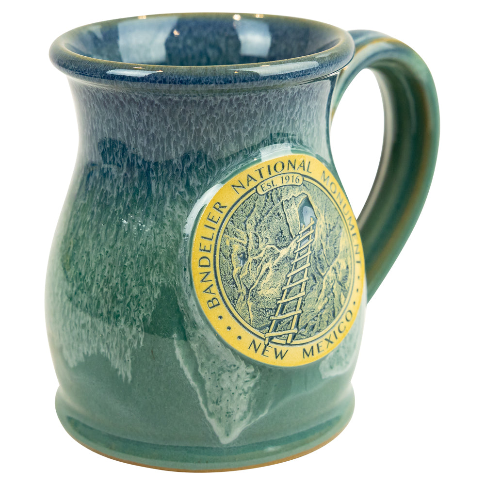 Teal ceramic mug with Bandelier National Monument logo on a white background