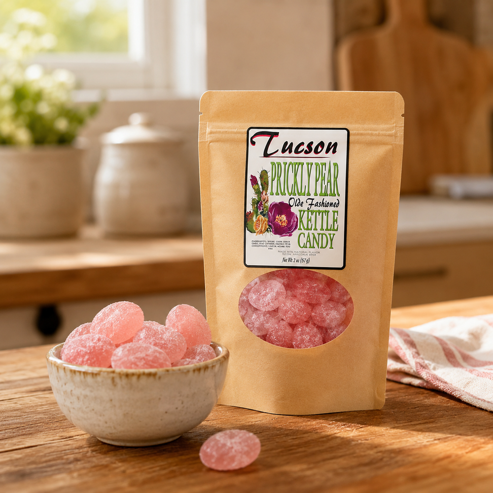 A stand-up pouch of Tucson prickly pear candy stands on a wooden table with a small bowl of pink candy pieces in front. The package label reads Tucson Prickly Pear Organic Kittle Candy, and the background shows a softly blurred kitchen setting.