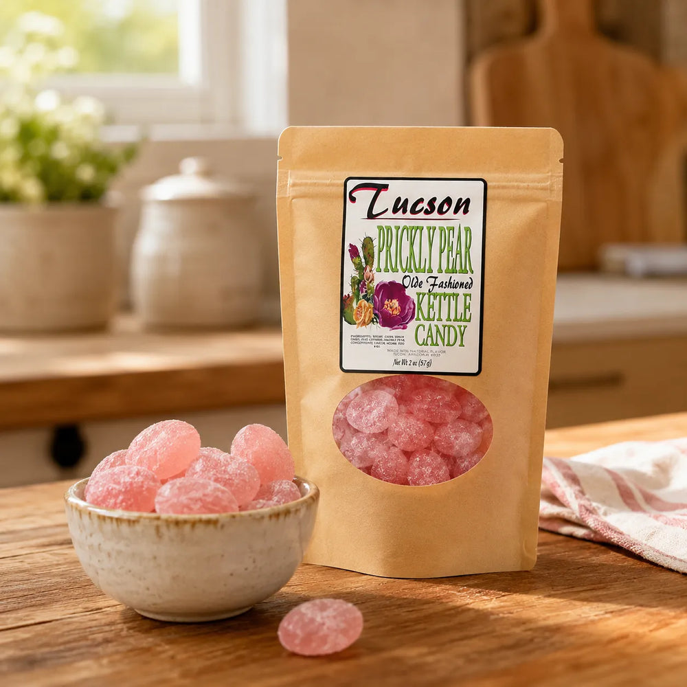 A stand-up pouch of Tucson prickly pear candy stands on a wooden table with a small bowl of pink candy pieces in front. The package label reads Tucson Prickly Pear Organic Kittle Candy, and the background shows a softly blurred kitchen setting.