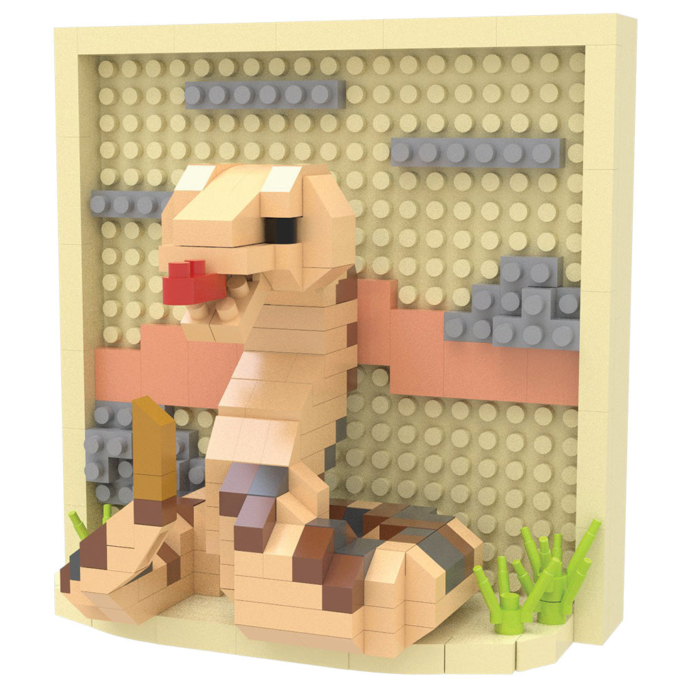 A toy building-block model of a rattlesnake constructed from tan, beige, brown, gray, pink, green, and red pieces, displayed against a cream-colored stud wall.