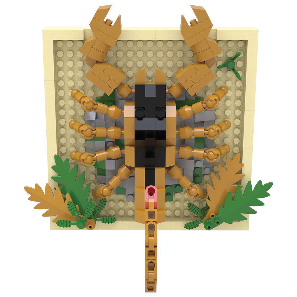 A toy building-block style scorpion figure mounted on a square beige base plate, with tan legs and claws, a black head, green leaves, and gray stone-like accents on a plain white background.