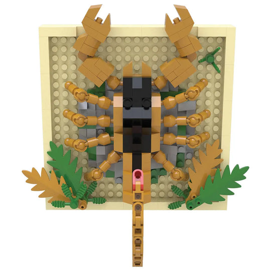 A toy building-block style scorpion figure mounted on a square beige base plate, with tan legs and claws, a black head, green leaves, and gray stone-like accents on a plain white background.