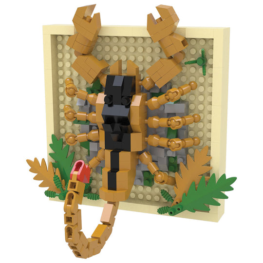 A toy building-block model of a scorpion mounted on a beige display board with green leaves and gray rock details, photographed on a plain white background.