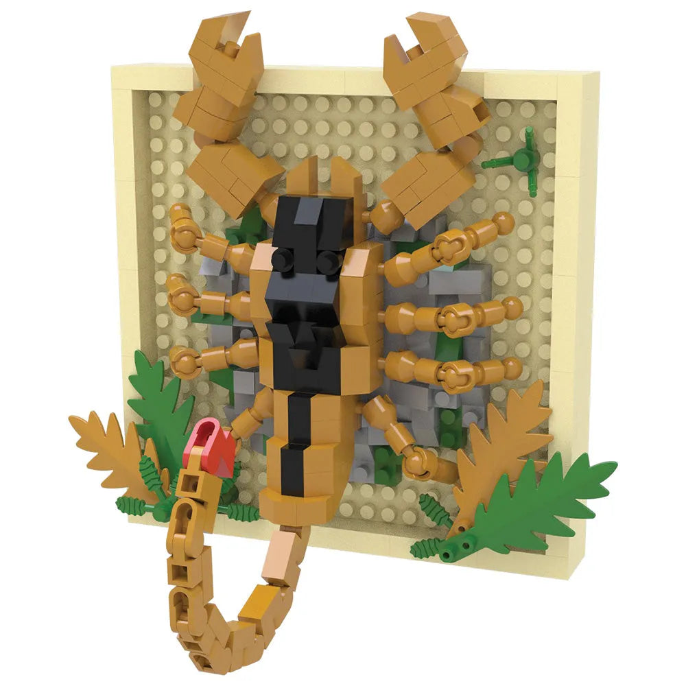 A toy building-block model of a scorpion mounted on a beige display board with green leaves and gray rock details, photographed on a plain white background.