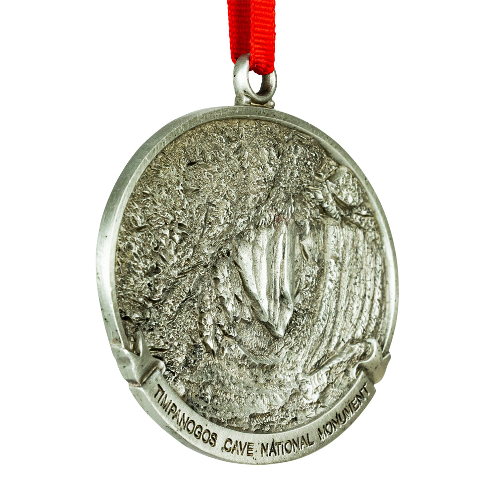 Pewter ornament with engraved design and red ribbon on a white background