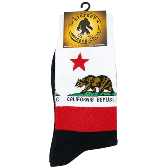 A pair of Bigfoot Sock Co. crew socks featuring a California Republic flag design with a white upper section, red star, brown grizzly bear, and red stripe, finished with a black toe and cuff.
