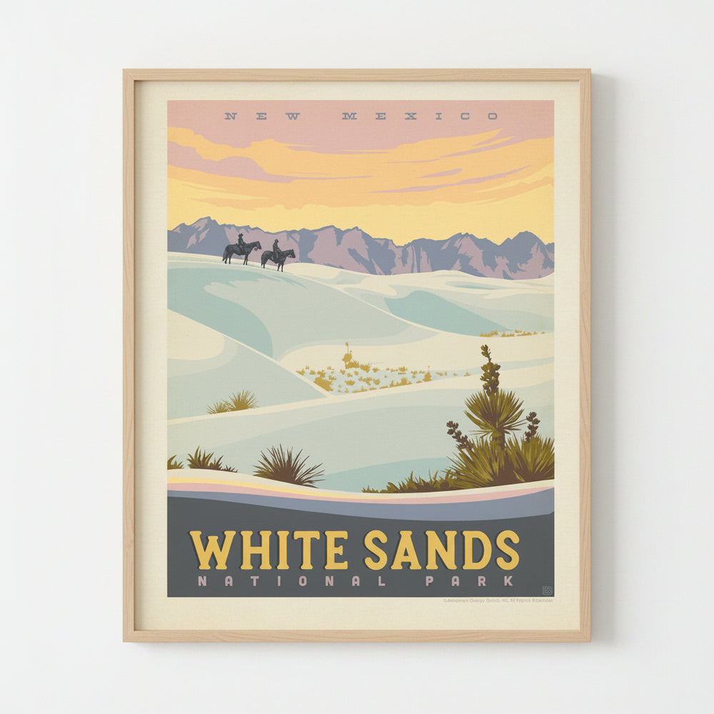 A vintage-style travel poster for White Sands National Park in New Mexico, showing pale blue-white sand dunes, distant purple mountains, and a warm yellow-orange sky, framed and mounted on a wall.