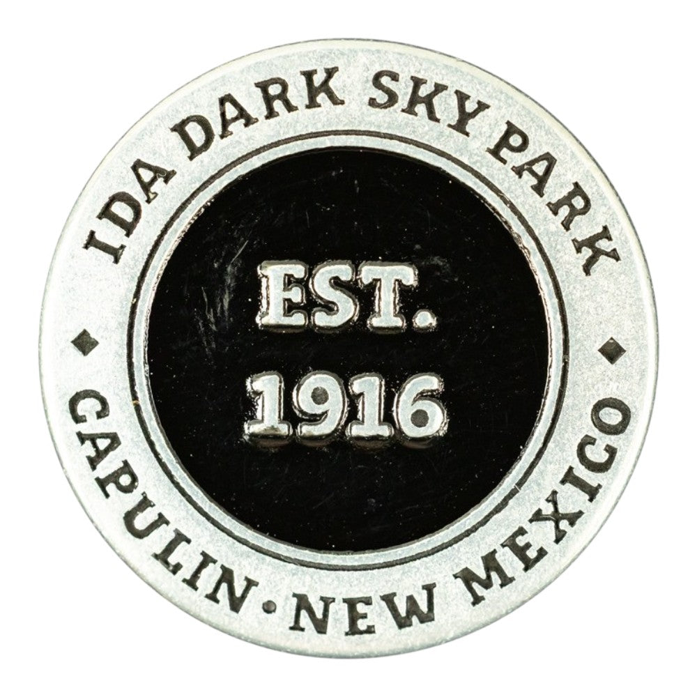 A circular metal commemorative token for Capulin Volcano National Monument in Capulin, New Mexico, established in 1916. The design features a silver-toned outer ring with engraved text and a black center with raised silver lettering.