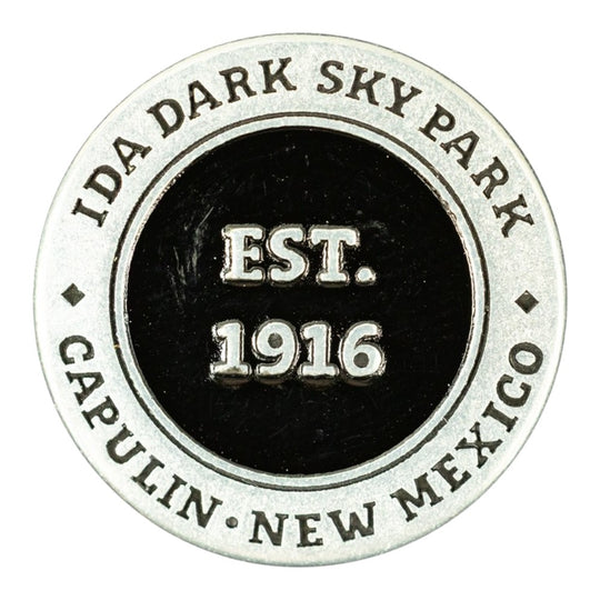 A circular metal commemorative token for Capulin Volcano National Monument in Capulin, New Mexico, established in 1916. The design features a silver-toned outer ring with engraved text and a black center with raised silver lettering.