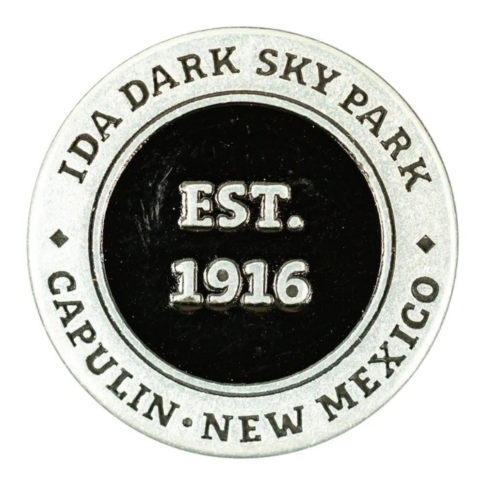 A circular metal commemorative token for Capulin Volcano National Monument in Capulin, New Mexico, established in 1916. The design features a silver-toned outer ring with engraved text and a black center with raised silver lettering.