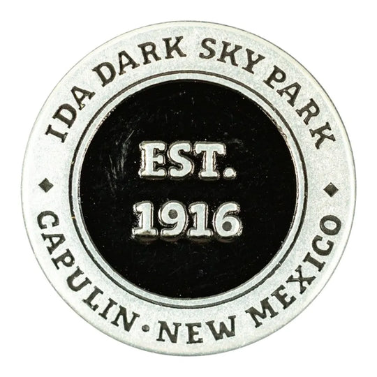 A circular metal commemorative token for Capulin Volcano National Monument in Capulin, New Mexico, established in 1916. The design features a silver-toned outer ring with engraved text and a black center with raised silver lettering.