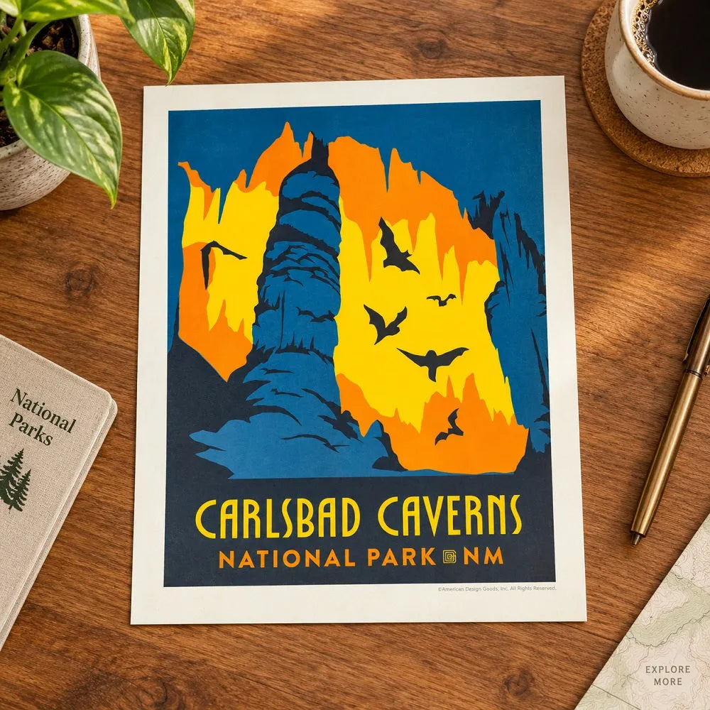 Graphic print representing CARLSBAD CAVERNS NATIONAL PARK NM laying flat on a wooden desk with plant, collee mug, and national park journal.