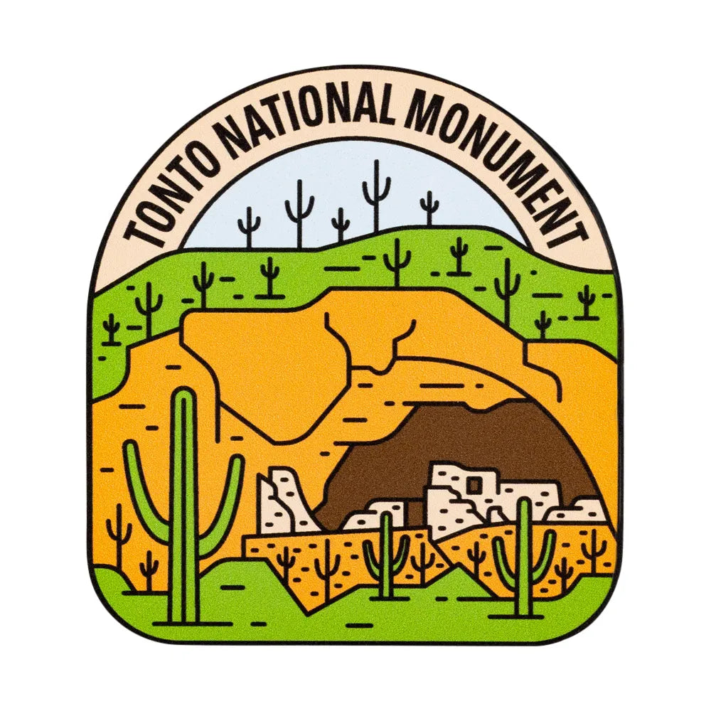 A stylized illustrated sticker reading 'TONTO NATIONAL MONUMENT' around an arched desert landscape scene with green cacti, yellow-orange rock formations, a brown cave, and small white buildings on a light gray background.